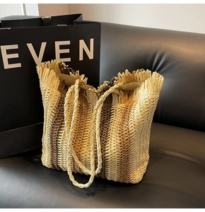 Detail of straw woven tote bag featuring natural fringe edges and slender shoulder straps
