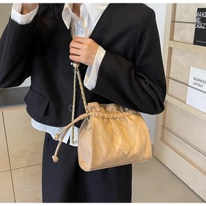 Quilted light brown bucket bag with metal chain strap worn by a model in a stylish setting