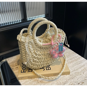 Detail of straw woven handbag with ring handles, drawstring liner, and flower charm