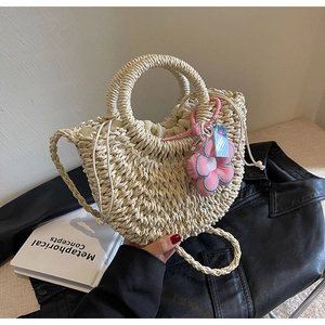 Close-up of beige woven straw moon bag with drawstring liner and pink floral charm