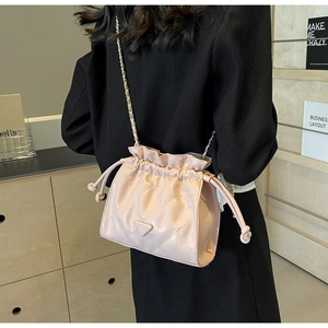 Detail of pink quilted bucket bag with chain strap worn over a black blazer jacket