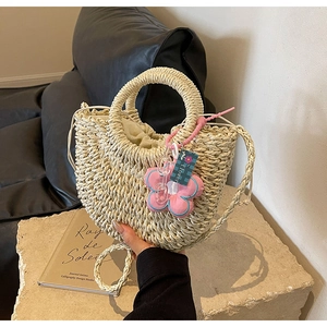 Detail of woven straw half-moon bag with cream drawstring liner and pink flower charm