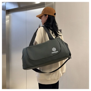 Olive green travel duffel bag with shoulder strap worn by a person in a minimalist setting