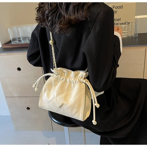 Quilted cream leather bucket bag with gold chain strap shown on a woman in a black blazer