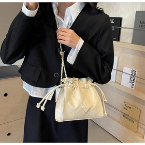 Detail of beige quilted bucket bag with chain strap and triangular plaque on shoulder