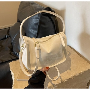 Détail du sac Boston crème avec logo embossé et boucle en métal sur pierre