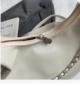 Close-up of cream tote bag featuring smooth silver zipper and textured leather detail