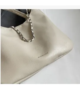 Detailed close-up of cream leather tote bag with lychee texture and chain detail