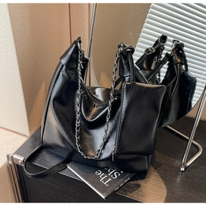 Detail of black glossy leather tote bag featuring a silver chain and small matching pouch