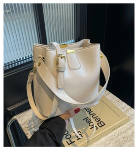 Gros plan d'un sac seau en cuir beige avec boucle dorée et bandoulière réglable