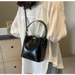 Détail du sac seau en cuir noir brillant avec fermoir magnétique doré et accessoires