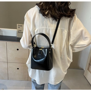 Détail d'un sac seau en cuir noir brillant avec des ferrures dorées porté par un mannequin