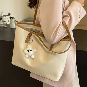 Minimalist cream tote bag with brown straps and plush charm shown on female model