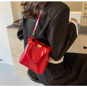 Sac seau en cuir rouge brillant avec boucles dorées porté avec un blazer noir