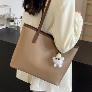 Khaki leather tote bag with long straps and cute bear charm shown in a warm cafe setting