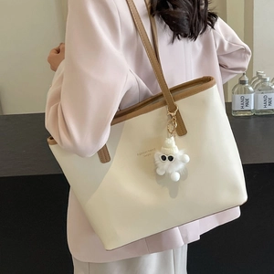 Minimalist creamy tote bag with brown trim and plush charm worn with a pink blazer
