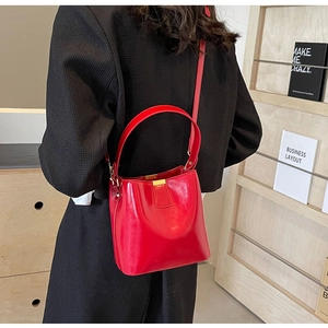 Sac seau rouge verni avec fermoir doré porté en bandoulière par un mannequin