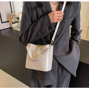 Détail d'un sac seau crème avec garnitures dorées porté en sac bandoulière minimaliste
