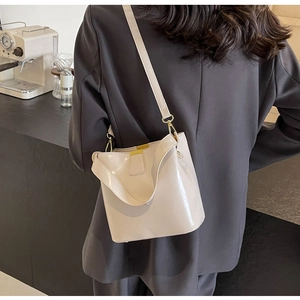 Détail d'un sac seau ivoire brillant avec des garnitures dorées porté par un mannequin