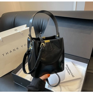 Détail du sac seau en cuir verni noir avec boucles dorées dans un coffret cadeau élégant