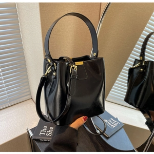 Sac seau en cuir noir brillant avec boucles dorées et poignée dans un décor minimaliste