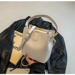 Détail du sac seau blanc avec garnitures dorées et bandoulière sur fond sombre