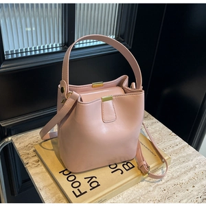 Détail du sac seau en cuir rose avec ferrures dorées posé sur un livre ancien