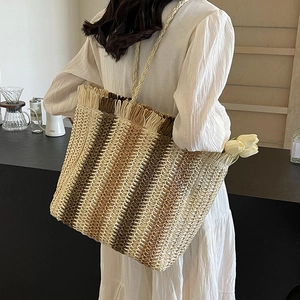 Large woven straw tote bag with gradient brown stripes and tassel trim for beach vacations