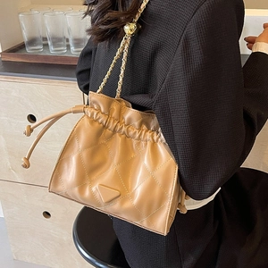 Chic quilted khaki bucket bag with gold chain strap shown on a model in a cozy setting