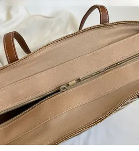 Détail d'un sac cabas en paille montrant la fermeture éclair et les anses en cuir