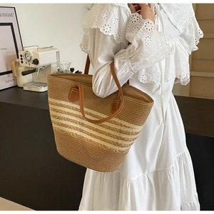 Détail d'un sac cabas rayé en paille avec anses en cuir dans un café au décor minimaliste