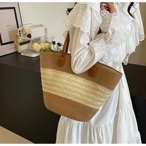 Détail d'un grand sac cabas rayé en paille avec anses en cuir marron porté par un mannequin
