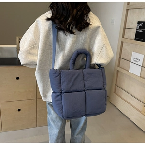Close-up of a dark blue quilted puffer tote bag worn on a model's shoulder for work