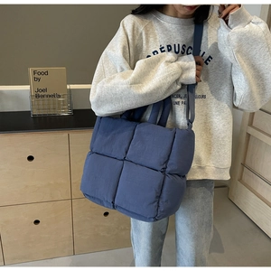 Detail of a large navy quilted tote bag worn crossbody in a modern home setting