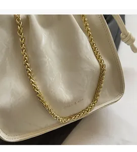 Detail of cream pleated bucket bag with gold chain strap and brand logo print