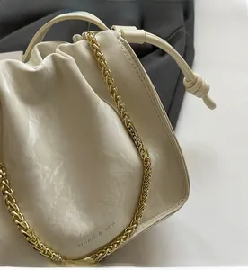 Detail of cream drawstring bucket bag with gold chain strap and pleated leather texture