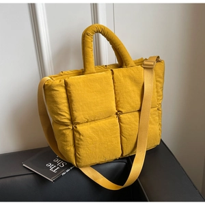 Detail of yellow quilted tote bag with padded handles and adjustable strap on leather sofa