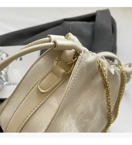 Close-up of glossy cream bucket bag with gold ring hardware and chain strap details