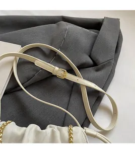 Detail of cream bucket bag showing adjustable leather strap and gold metal chain hardware