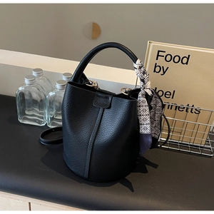 Detail of black lychee grain leather bucket bag with silk scarf and gold hardware