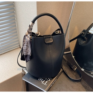 Close-up of black lychee leather bucket bag with decorative scarf and logo detail