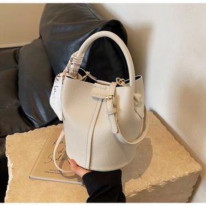 Close-up of beige lychee grain bucket bag with artistic scarf handle on stone base