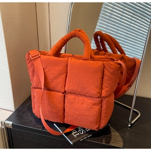 Close-up of orange quilted puffer tote bag with adjustable strap and padded handles
