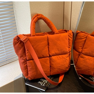 Close-up of bright orange quilted puffer tote bag showing padded nylon fabric texture