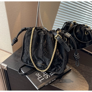 Detail of black drawstring bucket bag with textured pleats and golden chain strap