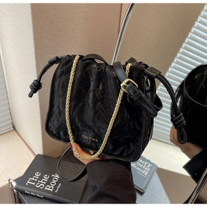 Detail of black pleated bucket bag showing drawstring closure and elegant gold chain strap