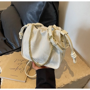 Detail of off-white pleated bucket bag with gold chain strap on a textured stone base