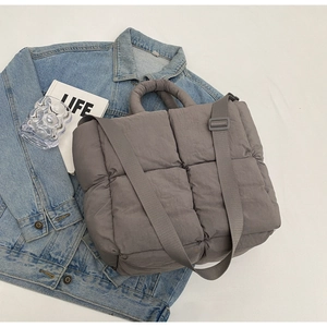 Detail of grey quilted tote bag showing padded texture and adjustable strap on denim