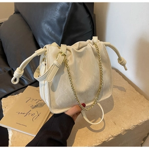 Detail of creamy white bucket bag with drawstring closure and golden chain on stone surface