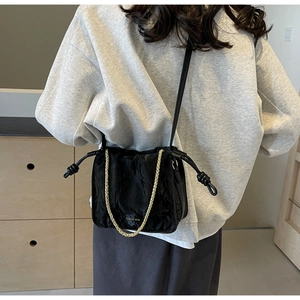 Detail of black pleated bucket bag with gold chain strap and drawstring closure